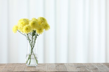 Wall Mural - Beautiful yellow flowers in vase on wooden table at home. Space for text