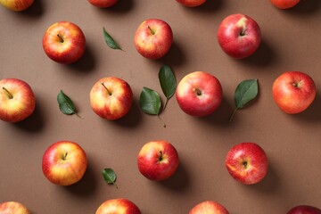 Wall Mural - Ripe red apples and green leaves on brown background, flat lay