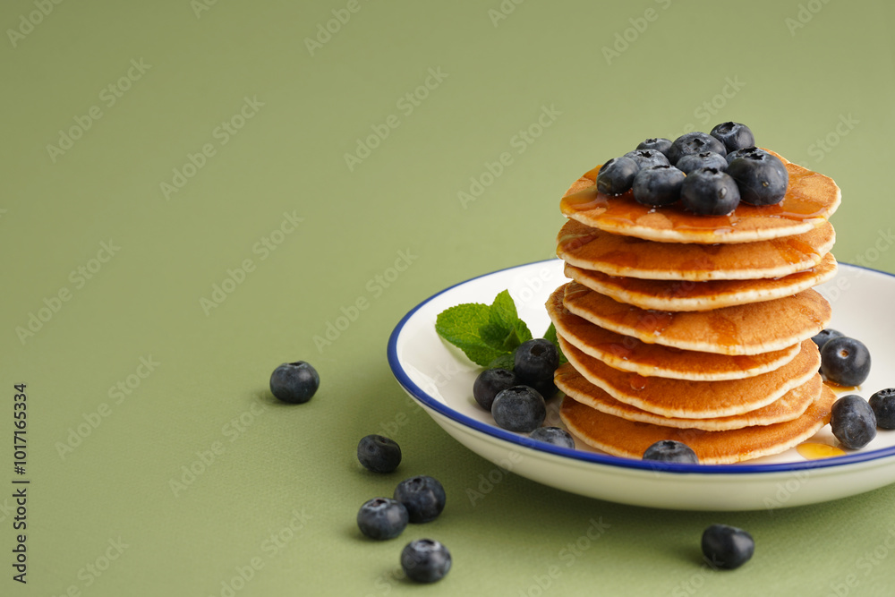 Plate with tasty pancakes and blueberries on green background