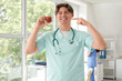 © Pixel-Shot - Young male doctor with apple pointing at his teeth in clinic
