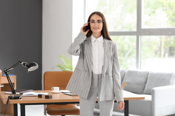 Wall Mural - Beautiful young happy businesswoman talking by mobile phone in office