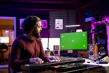 Leinwandbilder - Audio engineer learning to work on electronic keyboard in home studio, using mixing console and midi controller and watching tutorials. Producer playing piano notes, greenscreen display on pc.