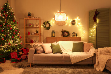 Sticker - Interior of festive living room with grey sofa, Christmas tree and glowing lights at evening