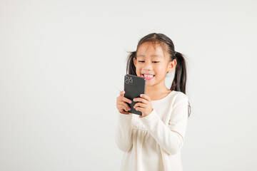 Happy Asian portrait cute young kid girl smiling excited using smart mobile phone studio isolated on white background, Thai kindergarten child surprised holding reading message gesture on smartphone