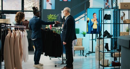 Wall Mural - Fashion stylist making trendy recommendations for senior client, pairing an expensive tie to match a black elegant shirt. African american worker selling designer items to man. Camera B.