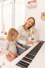 Little girl playing a piano with her mother