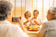 © CandyRetriever  - Happy Asian senior women friends having dinner together at home. Elderly retired woman enjoy indoor lifestyle using mobile phone taking picture during eating healthy food together on dining table.