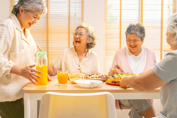 Group of Happy Asian senior women having dinner together at home. Elderly retired woman friends enjoy indoor lifestyle meeting party eating healthy food and vegetables salad together on dining table.