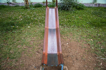 A rusty metal slide sits in a grassy park, waiting for children to come and enjoy the fun. The slide is old and weathered, but still looks like it could be used for playtime.