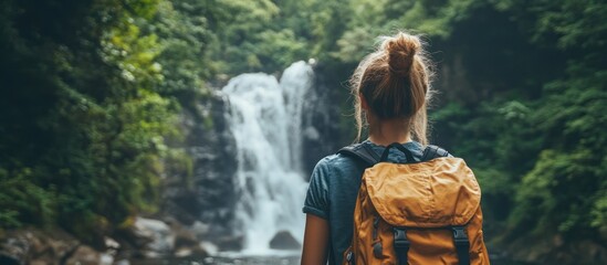 Wall Mural - a young woman stands in a lush green forest, admiring a cascading waterfall.