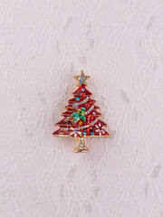 Close-up of a bright beautiful brooch in the form of a red  Christmas tree on a light background