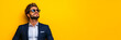 © Vertigo Images - Man in suit and sunglasses looks up against a yellow background.