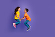 © deagreez - Full length photo of lovely two little kids hold hands jumping dressed stylish orange yellow garment isolated on purple color background