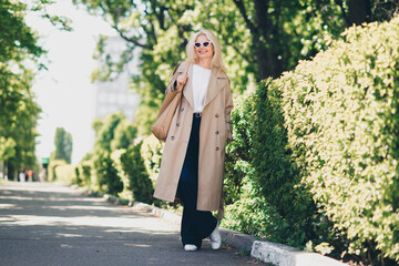 Wall Mural - Full length photo of cheerful happy retired woman walking smile spring good mood weekend wear beige coat enjoy outdoors outside park street