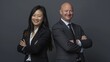 © MD Media - Photo of two happy diverse professional people, smiling at the camera, wearing a business suit dressed in a grey. multi ethnic business couple posing arms crossed copy space and new isolated