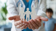 © KirKam - Doctor holds paper family cutout, smiling. Office background. Symbolizes family-centered care, healthcare provider connection with patients.