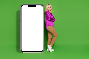 Wall Mural - Full body photo of nice senior female point big smartphone crossed hands wear trendy violet satin outfit isolated on green color background