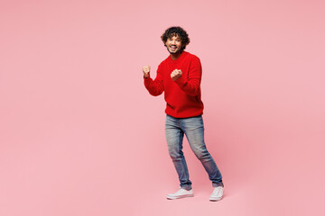 Poster - Full body young Indian man he wear red sweater casual clothes doing winner gesture celebrate clenching fists say yes isolated on plain pastel light pink background studio portrait. Lifestyle concept.