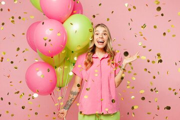 Canvas Print - Young shocked surprised woman wear shirt celebrating birthday holiday stand near bunch of colorful air balloons look at confetti glitters rainfall isolated on plain pink background. Lifestyle concept.