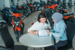 © Odua Images - female customer looking at a list of motorcycle types with a Muslim woman shop assistant in the showroom