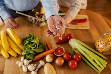 Close up of senior couple's hands holding pills above table full of healthy food.