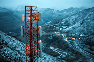 a red telecommunications tower with various antennae in a mountainous snowy landscape, with lights f