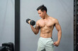 © chadchai - A physically fit man engaged in a workout session at a modern gym, determinedly lifting a heavy dumbbell as he strives for strength and wellness.