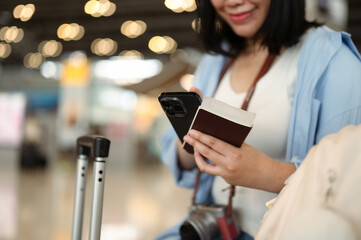 Cropped shot of smiling young woman holding passport and using mobile phone in airport lounge