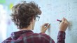 © ShaZi - Back view of high school student solving math problem on whiteboard in classroom. Young man writing math solution on white board using marker. College guy solving math expression during lesson.