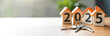 © Olga - Keys to a new house and wooden models of mini-houses with numbers for the New Year 2025 on the table. The concept of housing, real estate market, investments. Panoramic banner with copy space