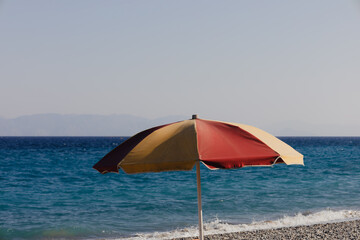 Minimalism relaxing travel background in vintage colors. One red and yellow beach umbrella on sandy sea coast in early morning. Copy space for your text. Holiday vacation on the seaside.