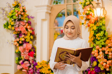 Beautiful adult woman indonesia hijab wearing white muslim dress smiling to quran both hands holding book, open quran in luxury interior. for fashion, promotion, lifestyle, religious content