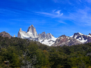 Fitz Roy rugged mountain ridge viewpoint behind green forest midday clear skies