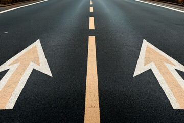 Canvas Print - Close-up of a two-way asphalt road with double yellow lines and directional arrows indicating left and right lanes, symbolizing bidirectional traffic.