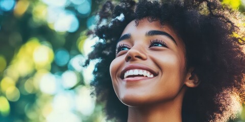 Joyful woman with curly hair smiles brightly in nature, exuding happiness and positivity. Perfect for lifestyle and wellness themes.