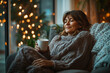 © okrasiuk - Middle aged woman relaxing with cup of hot drink sits comfortably by the window, wrapped in cosy knitted sweater and admiring the snow-covered landscape outside. Lady dreaming. Cozy winter at home.