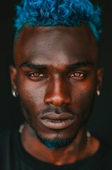 Close-up portrait of a handsome African American man with dyed blue hair and brown eyes on black background.