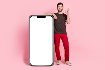 Poster - Full size photo of optimistic man dressed t-shirt lean on smartphone display empty space show okey isolated on pink color background