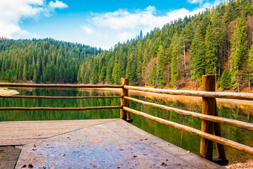 wooden pier on the lake synevyr in autumn. mountain landscape on a sunny day. scenery reflecting in the water. european woodland