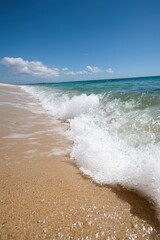 Poster - A serene beach scene with gentle waves lapping against golden sand under a bright blue sky, perfect for relaxation and nature photography.