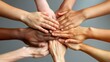 © Suradet Rakha - Close-up of young people's hands together in teamwork on a grey background, top view. Conceptual photo for teamwork, community support, or friendship.