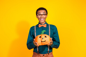 Canvas Print - Portrait of nice elegant young man hold carved halloween pumpkin isolated on yellow color background