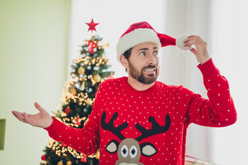 Canvas Print - Photo of nice young man look festive hat pompom ugly sweater christmas time apartment indoors