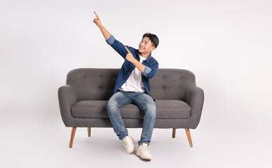 Full body image of young Asian man posing on sofa on white background