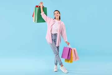 Smiling woman with colorful shopping bags on light blue background