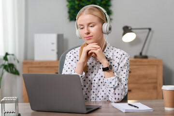 Canvas Print - Interpreter in headphones working with laptop at table indoors