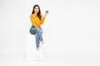 © comzeal - Happy young Asian woman sitting on white box and showing credit card isolated on white background