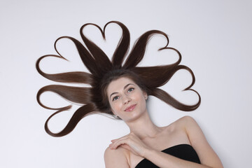 Poster - Beautiful young woman with hair in shape of hearts on white background, top view