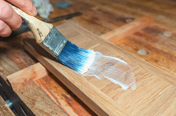 carpenter applies glue to surface of board with brush in carpentry workshop