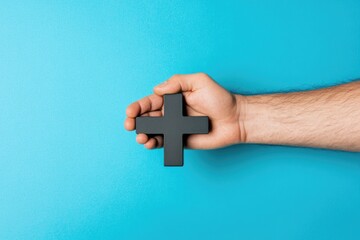 Poster - A close-up of a hand holding a black cross against a bright blue background, symbolizing faith and spirituality